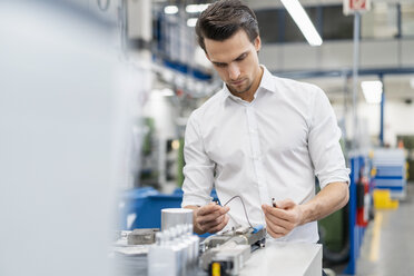 Geschäftsmann bei der Prüfung eines Werkstücks in einer Fabrik - DIGF05770