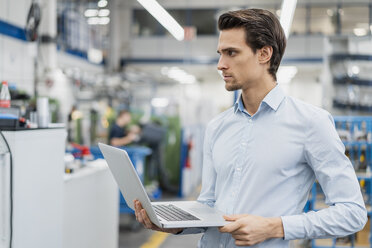 Portrait of businessman holding laptop in a factory - DIGF05791