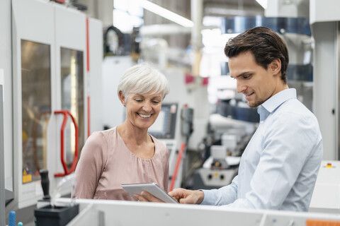 Lächelnder Geschäftsmann und ältere Frau mit Tablet im Gespräch in einer Fabrik, lizenzfreies Stockfoto