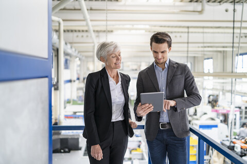 Geschäftsmann und ältere Geschäftsfrau mit Tablet im Gespräch in einer Fabrik, lizenzfreies Stockfoto