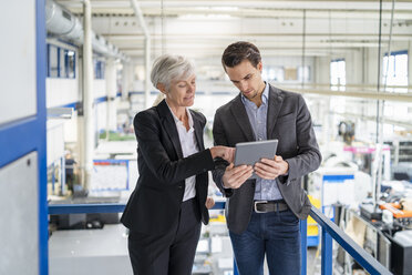 Businessman and senior businesswoman with tablet talking in a factory - DIGF05802