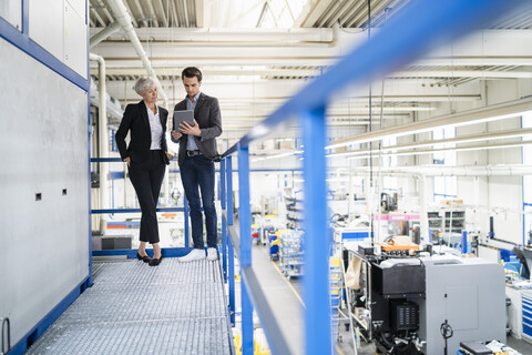 Businessman and senior businesswoman with tablet talking in a factory stock photo