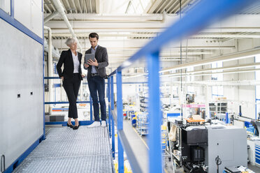 Businessman and senior businesswoman with tablet talking in a factory - DIGF05803