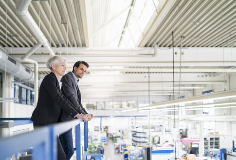 Ältere Geschäftsfrau und Geschäftsmann im oberen Stockwerk einer Fabrik mit Blick auf den Verkaufsraum - DIGF05804