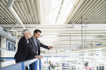 Senior businesswoman and businessman on upper floor in factory overlooking shop floor - DIGF05805