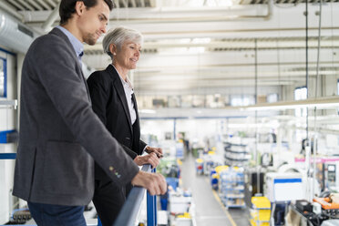 Senior businesswoman and businessman on upper floor in factory overlooking shop floor - DIGF05808