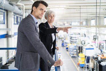 Ältere Geschäftsfrau und Geschäftsmann im oberen Stockwerk einer Fabrik mit Blick auf den Verkaufsraum - DIGF05810