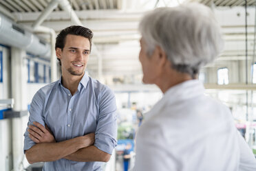 Smiling businessman talking to senior businesswoman in a factory - DIGF05814