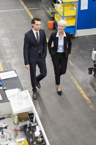 Geschäftsmann und ältere Geschäftsfrau gehen in einer Fabrik, lizenzfreies Stockfoto