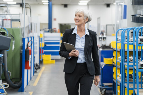 Senior businesswoman with tablet walking in a factory - DIGF05821