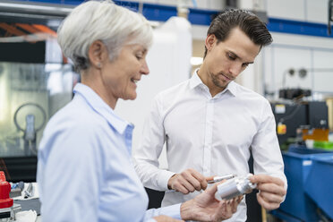 Businessman and senior businesswoman examining workpiece in a factory - DIGF05823