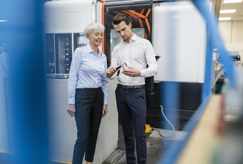 Geschäftsmann und ältere Geschäftsfrau messen ein Werkstück in einer Fabrik, lizenzfreies Stockfoto