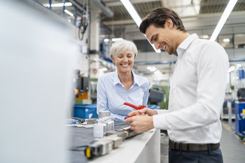 Ein glücklicher Geschäftsmann und eine ältere Geschäftsfrau begutachten ein Werkstück in einer Fabrik - DIGF05829