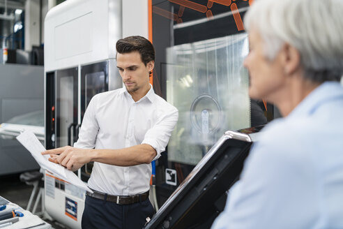 Geschäftsmann und ältere Geschäftsfrau mit Handbuch an einer Maschine in einer Fabrik - DIGF05831