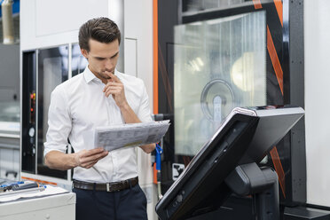 Businessman reading manual at a machine in a factory - DIGF05835
