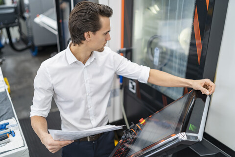 Geschäftsmann mit Handbuch an einer Maschine in einer Fabrik, lizenzfreies Stockfoto