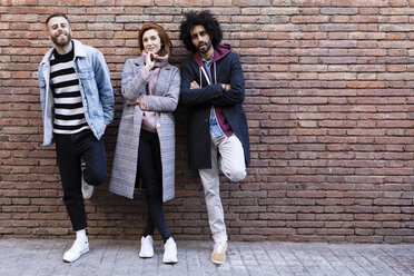 Portrait of three friends standing at a brick wall - JRFF02615