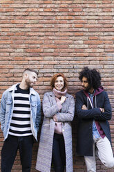 Portrait of three friends standing at a brick wall - JRFF02616
