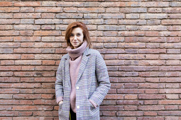 Porträt einer lächelnden jungen Frau, die an einer Backsteinmauer steht - JRFF02619