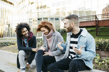 Drei glückliche Freunde sitzen in der Stadt und unterhalten sich - JRFF02624