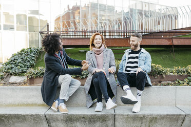 Drei glückliche Freunde sitzen in der Stadt und unterhalten sich - JRFF02626