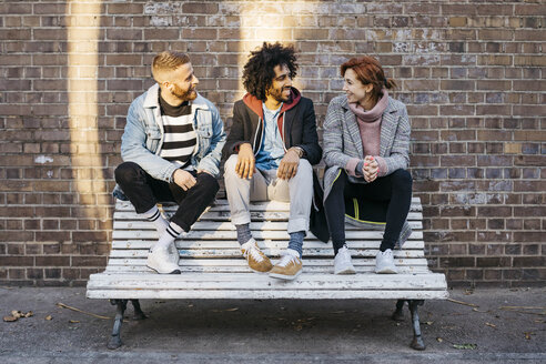 Drei Freunde unterhalten sich auf einer Bank vor einer Backsteinmauer - JRFF02632