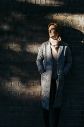 Young woman standing at a brick wall in shadow looking sideways - JRFF02639