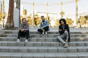 Portrait of three serious friends sitting on stairs - JRFF02646