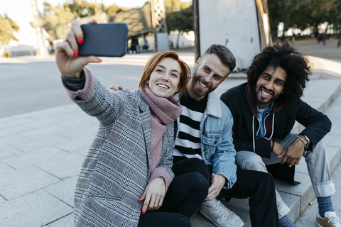 Drei glückliche Freunde sitzen im Freien und machen ein Selfie, lizenzfreies Stockfoto