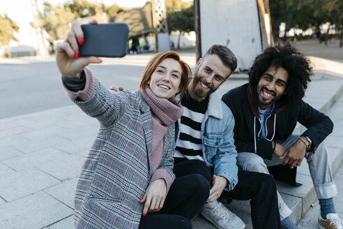 Drei glückliche Freunde sitzen im Freien und machen ein Selfie - JRFF02650