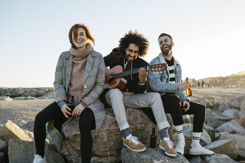 Drei glückliche Freunde mit Gitarre sitzen bei Sonnenuntergang im Freien - JRFF02653