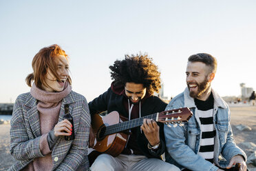 Drei glückliche Freunde mit Gitarre sitzen bei Sonnenuntergang im Freien - JRFF02654