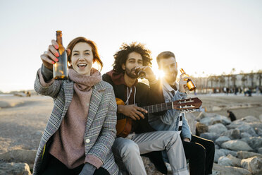 Three happy friends with guitar toasting beer bottles at sunset - JRFF02657