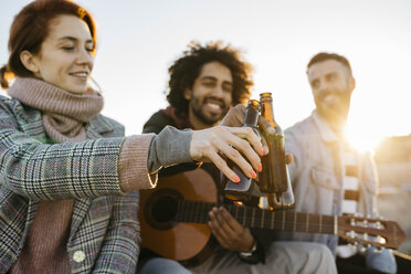 Three happy friends with guitar toasting beer bottles at sunset - JRFF02658