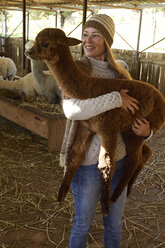 Portrait of smiling mature woman carrying young alpaca in her arms - ECPF00502