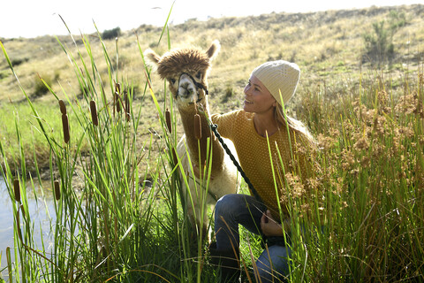 Lächelnde reife Frau mit angeleintem Alpaka in der Natur, lizenzfreies Stockfoto