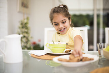 Glückliches kleines Mädchen nimmt einen Keks beim Frühstück zu Hause - ABZF02226