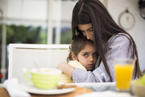 Mother embracing her sad daughter during breakfast at home stock photo