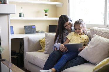 Glückliche Mutter und Tochter sitzen zu Hause auf der Couch und benutzen ein Tablet - ABZF02235