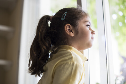 Kleines Mädchen zu Hause, das aus dem Fenster schaut, lizenzfreies Stockfoto