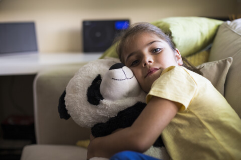 Kleines Mädchen liegt zu Hause auf der Couch und kuschelt mit einem Panda-Teddybär, lizenzfreies Stockfoto