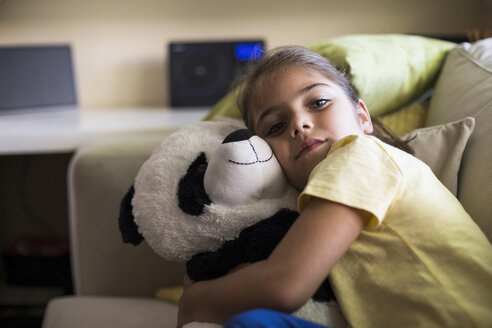 Kleines Mädchen liegt zu Hause auf der Couch und kuschelt mit einem Panda-Teddybär - ABZF02239