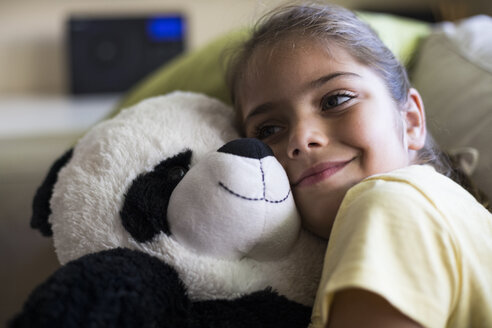 Kleines Mädchen liegt zu Hause auf der Couch und kuschelt mit einem Panda-Teddybär - ABZF02240