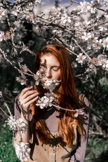 Rothaarige Frau riecht an Baumblüten - AFVF02385