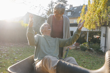Glückliches älteres Paar hat Spaß mit Schubkarre im Garten - KNSF05504