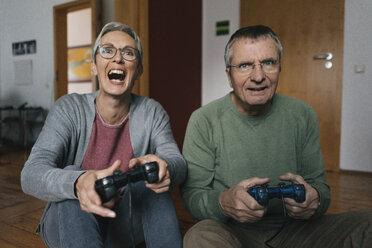 Excited senior couple playing video game at home - KNSF05507