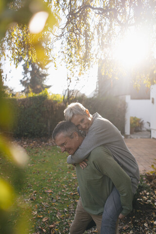 Glücklicher älterer Mann trägt Frau huckepack im Garten, lizenzfreies Stockfoto