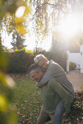 Happy senior man carrying wife piggyback in garden - KNSF05509