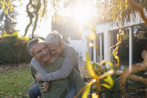 Glücklicher älterer Mann trägt Frau huckepack im Garten, lizenzfreies Stockfoto