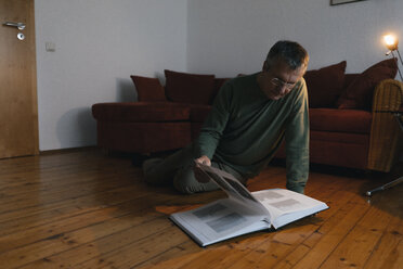 Älterer Mann sitzt zu Hause auf dem Boden und betrachtet ein Fotoalbum - KNSF05531